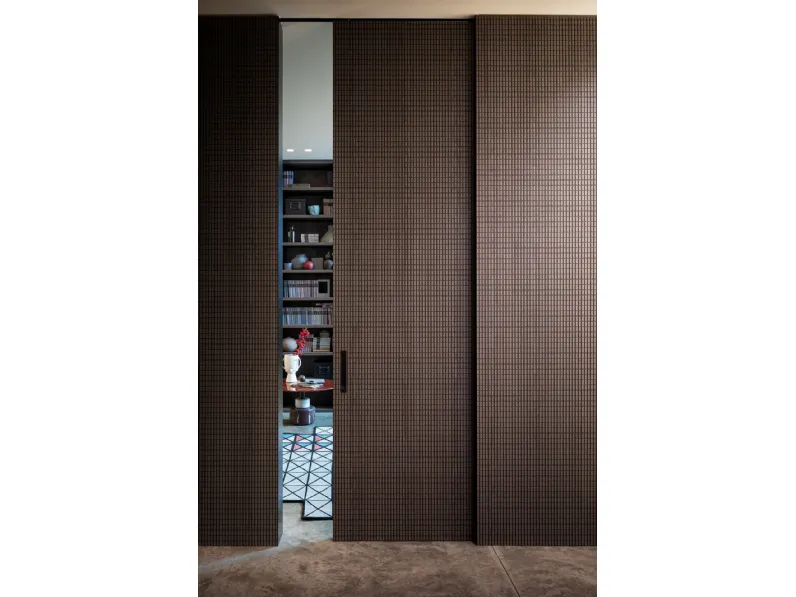 Porta per interni scorrevole con intaglio dalle geometrie tridimensionali ripetuto identico sulle pareti Chocolat di Lualdi